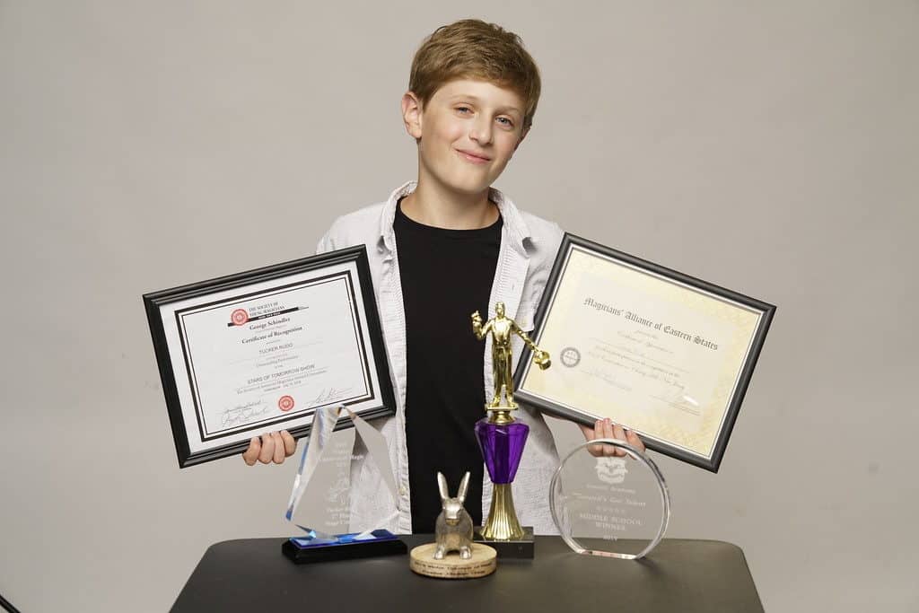 A boy holding two awards and one trophy.